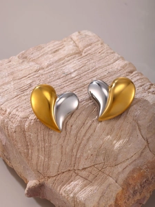 Macro shot of two-tone polished heart stud earrings on a textured stone display