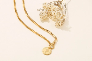 Detail of gold coin necklace with mixed Cuban and paperclip chains on beige background