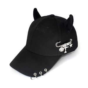 Detail of black baseball cap with devil horns, silver metal rings and pin charms