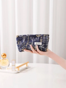 Floral embroidered navy cotton linen makeup bag held against a minimal home background