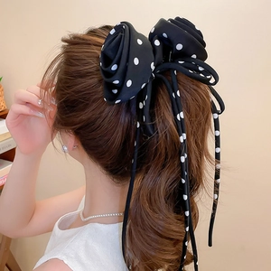 Close-up of black and white polka dot bow hair tie with silk texture and long ribbons