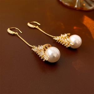 Détail de boucles d'oreilles perles dorées avec zircons sur fond de cuir marron riche