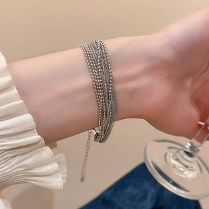 Detail of layered silver beaded chain bracelet worn with elegant white ruffled sleeves