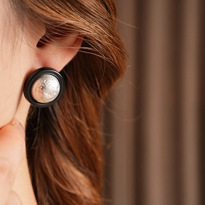 Close-up of circular vintage stud earring featuring black matte rim and silver relief texture