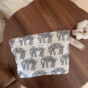 Flat lay of an embroidered sheep canvas makeup bag with a Simple Wish label on wood