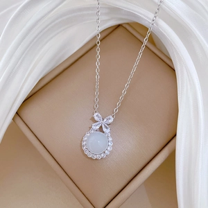 Close-up of a silver bow necklace with white gemstone pendant on elegant white silk