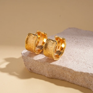 Close-up of 18K gold-plated ribbed hoop earrings resting on a natural stone surface
