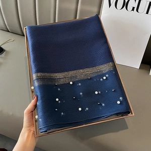Close-up of navy silk scarf featuring pearl beads and gold stripes in a metal tray