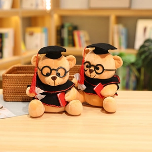 Pair of graduation teddy bears with black caps and robes on a warm wooden desk