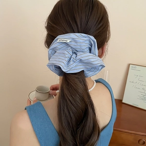 Detailed view of blue and white striped cotton fabric scrunchie with logo tag