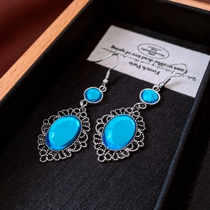 Dettaglio ravvicinato di orecchini vintage in resina blu in un portagioie di legno e velluto