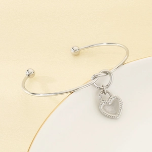 Detail shot of silver knot heart pendant bangle on a minimalist white display tray