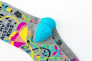 Detail of grey knitted novelty socks with colorful floral patterns and LOVE MY ASSHOLE KIDS text