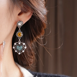 Close-up of vintage drop earring with round crystals, yellow gem, heart diamond and pearl