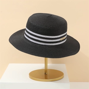 Close-up of black straw sun hat with white stripes and a refined gold metal plaque