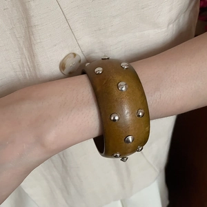Gros plan d'un large bracelet en bois vintage avec des clous argentés sur lin beige