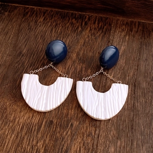 Detailed view of U-shaped earrings featuring blue resin, gold chains, and white pleats