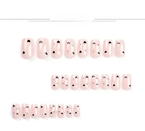 Close-up of nude pink press-on nails with black heart patterns and colorful rhinestones