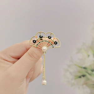 Detail of fan-shaped golden brooch with pearls and hanging chain tassel in vintage style