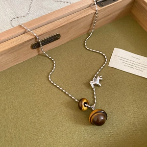 Detailed shot of retro tiger eye stone necklace with silver horse pendant on green fabric