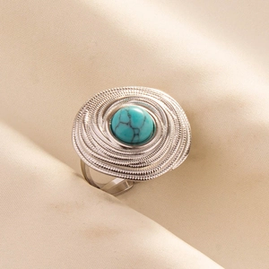Macro shot of turquoise stone ring with spiral metal layers on beige fabric