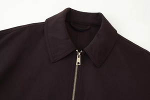 Detail of shark-shaped metal zipper pull on a dark collared jacket with woven fabric