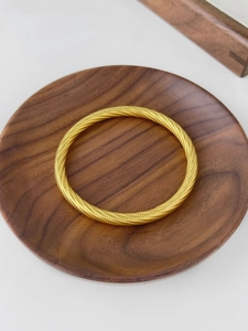 Detail of gold plated bangle featuring high quality spiral texture on wooden surface