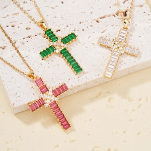 Three elegant gold necklaces with green, pink, and white zircon cross pendants on white stone