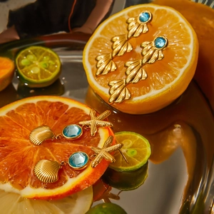 Detail of gold seashell earrings with blue gems placed on citrus slices in a creative macro shot