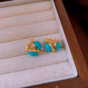 Macro detail of vintage gold hoop earrings with turquoise resin beads on beige velvet