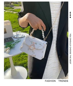 Close-up of white crossbody bag featuring pink floral embroidery and pearl handle