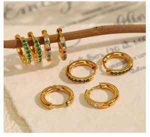 Detail of gold-plated earrings with multi-colored cubic zirconia stones on textured paper