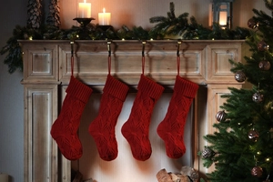 Set of four red knitted Christmas stockings hanging on a festive decorated fireplace mantel