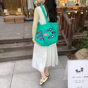 Green canvas tote bag with floral embroidery shown in a casual outdoor cafe setting