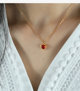 Detail of a red heart-shaped gemstone pendant on a fine gold chain worn on neck