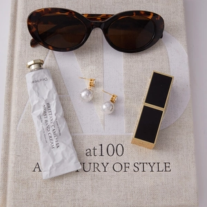 Flatlay-Ansicht von goldenen Perlenohrringen mit Zirkonia neben Sonnenbrille und Make-up