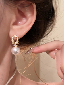 Close-up of sparkling zircon horseshoe earring with white pearl on model's ear