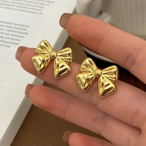 Detailed macro view of gold bow earrings with elegant textured finish held by hand
