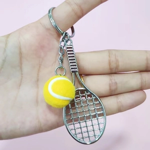 Detailed close-up of a mini yellow tennis ball and silver racket keychain on pink background