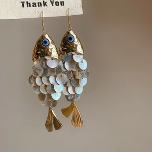 Close-up of ethnic fish-shaped earrings with shell scales and golden metal accents