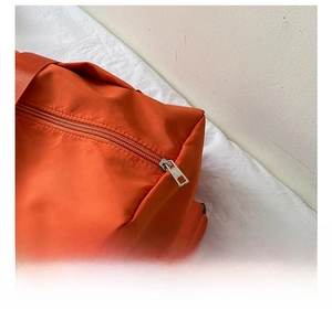 Close-up of durable silver hardware zipper pull on vibrant orange oxford fabric bag