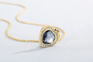 Macro shot of a heart-shaped deep blue crystal pendant with diamond halo on gold chain