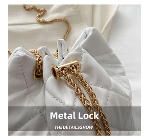 Close-up of golden metal lock and chain on white quilted leather bucket bag