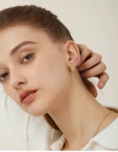 Close-up of lifestyle model wearing gold twisted hoop earrings and a delicate chain necklace