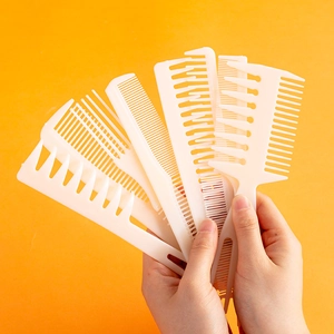 Hand holding set of 6 white plastic hair combs in fan shape on bright orange background