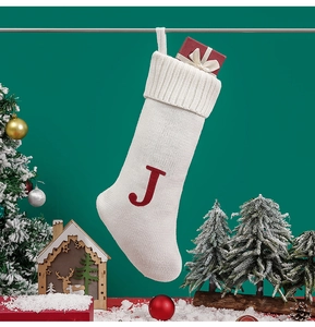 Macro detail of white knitted Christmas stocking with red letter J and gift box