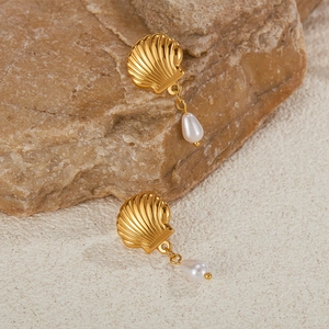 Macro shot of gold shell earrings with teardrop pearl drops on a natural stone background