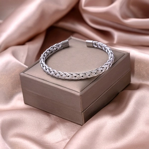 Detailed view of silver braided open cuff bracelet on a gift box with satin background
