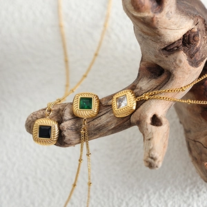 Retro gold necklaces with emerald and crystal square pendants displayed on rustic wood