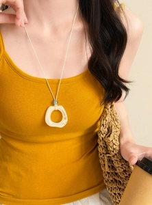 Close-up detail of a long necklace with cream marbled resin pendant and blue bead